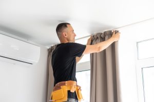 Image of a professional installing curtains on a window.